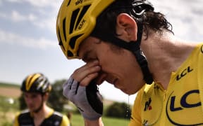 Great Britain's Geraint Thomas, wearing the overall leader's yellow jersey, cleans his stinging eyes after tear gas was used during a farmers' protest who attempted to block the stage's route.