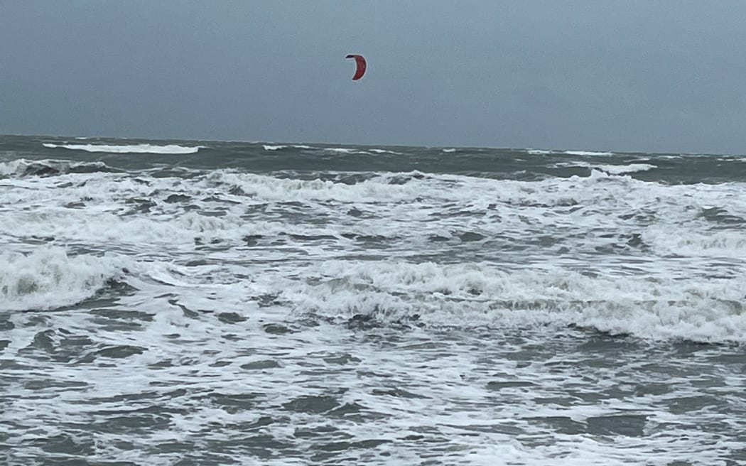 强风和涨潮冲走了奥克兰北部奥雷瓦海滩的一部分。 一名风筝冲浪者在汹涌的海浪中出海。