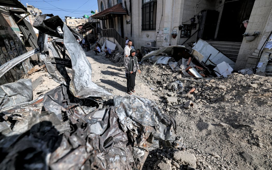 People stand by rubble and the remains of a destroyed vehicle outside a mosque in the occupied West Bank city of Jenin on 5 July 2023, after the Israeli army declared the end of a two-day military operation in the area.