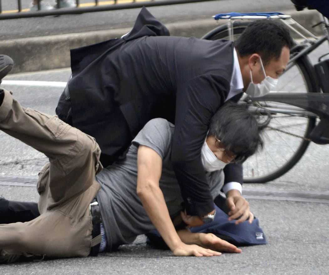 A man suspected of shooting Japanese Prime Minister Shinzo Abe at Yamato Saidaiji Station in Nara Prefecture on July 8, 2022 is wrestled to the ground.  67-year-old Abe has reportedly been shot in the chest during a stumping tour in Nara in the morning on July 8.