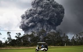 A man drives a golf cart at a golf course as an ash plume rises in the distance from the Kilauea volcano on Hawaii's Big Island on May 15, 2018