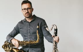 Saxophonist and bass clarinetist Dave Wilson sitting on a tall stool holding his instruments