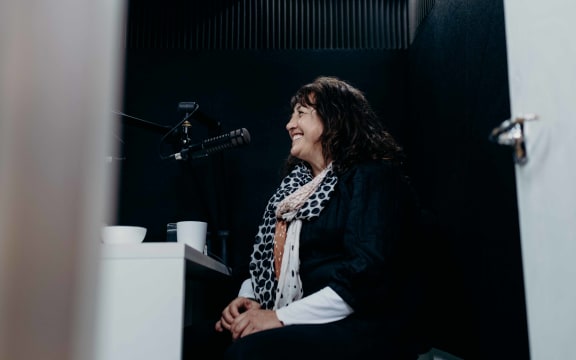 Carmen Parahi, Stuff journalist, smiles as she sits in a recording studio for the re_covering podcast.