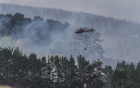 A helicopter flies in a load of water in a monsoon bucket during fire fighting efforts last Thursday in the Port Hills during the Christchurch fires. 16 February 2017