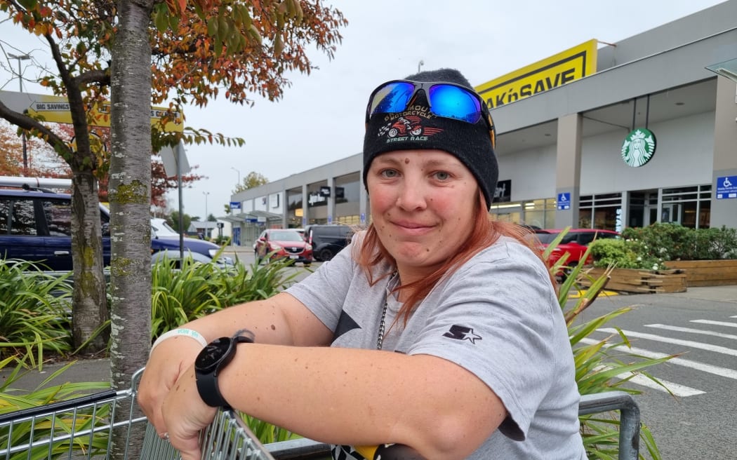 Olivia Bovey stands outside a supermarket leaning against a trolley. She is wearing a grey t-shirt, black beanie and has sunglasses on top of her head.