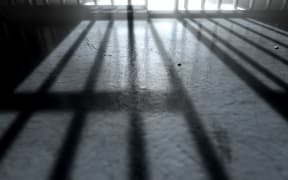 A 3D render of a closeup of view of a jail cells iron bars with an open door casting shadows on the prison floor with copy space