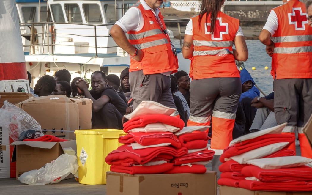 Migrants rest on the pier next to Red Cross agents after disembarking from a 'cayuco' (wooden boat) following a rescue operation on July 4, 2023 at the port of Los Cristianos, in the municipality of Arona, in the south of Tenerife, on the Spanish Canary island of Tenerife. A boat with 157 migrants on board, two of them women, has arrived on July 4, 2023 at the port of Los Cristianos, in the municipality of Arona, in the south of Tenerife, on the Spanish Canary island of Tenerife, Red Cross sources have reported. The vessel was located through the Integrated External Surveillance System (SIVE) when it was about 8 miles from the Punta Rasca area, and the Maritime Rescue's vessel Salvamar Alpheratz came out to meet it. The Salvamar Alpheratz accompanied the boat to the port of Los Cristianos, where it arrived at around 4:00 p.m. on July 4, 2023. (Photo by DESIREE MARTIN / AFP)