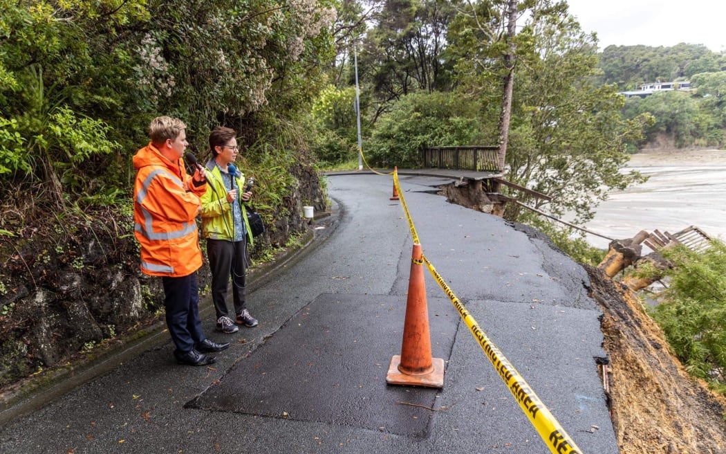 Auckland councillor Shane Henderson and Detail co-host Sharon Brettkelly wearing hi-vis, standing on the side of a damaged road.