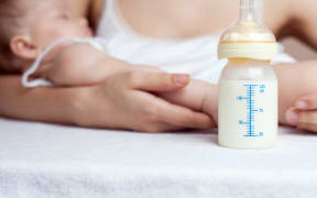 A mother holds a baby next to a bottle of milk.