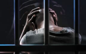 A man behind prison bars holds his head in his hands (stock photo).