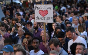 People attending a vigil at Albert Square in Manchester hold a sign 'Peace + Love Manchester.
