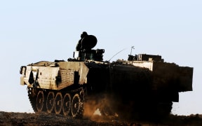 Army soldier on a moving heavily armored personnel carrier.