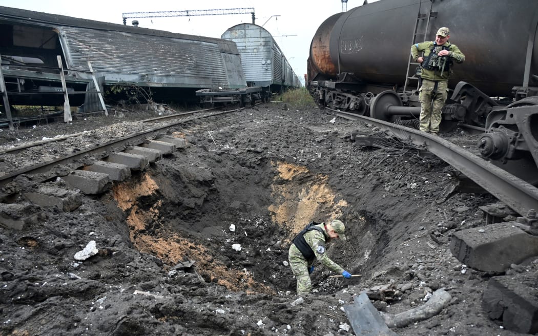 A forensic explosives expert examines a crater from a missile explosion at a freight railway station in Kharkiv, 21 September 2022, amid Russia's military invasion on Ukraine.