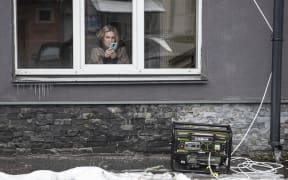 KYIV, UKRAINE - NOVEMBER 21: A woman is on her phone behind a generator as the power is out in Kyiv, Ukraine on November 21, 2022. As the Russian forces hit energy infrastructures since October, Ukrainian shops are obliged to use generators in order to stay in business. Power outages take place as the repair of the energy infrastructures continue intensively. Metin Aktas / Anadolu Agency (Photo by Metin Aktas / ANADOLU AGENCY / Anadolu Agency via AFP)