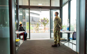 A security guard and soldier guarding an entrance to the M-Social Hotel, which is being used as a managed isolation facility, in Auckland.
