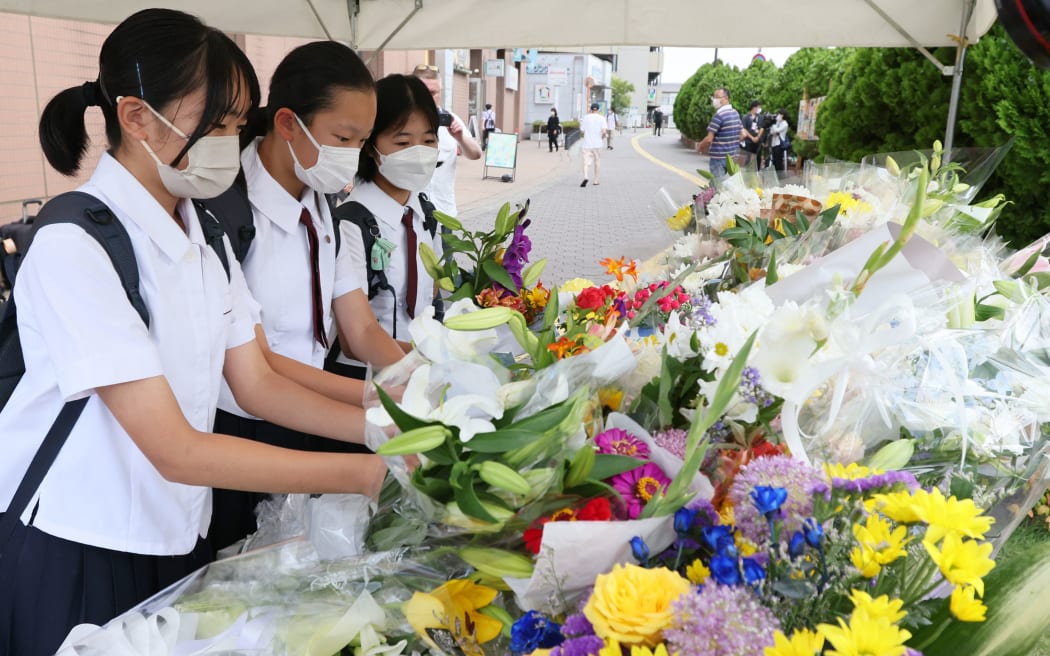 People offer flowers and prayers near a site where former Prime Minister Shinzo Abe was shot to death near Yamato Saidaiji Station in Nara Prefecture on July 9, 2022.Former Prime Minister Shinzo Abe was the victim of a fatal gun attack while taking part in a campaign event for the House of Councillors election in Nara City on the same day. He was 67. After being shot at around 11:30 a.m., he was confirmed dead at 5:03 p.m. at Nara Medical University Hospital in Kashihara, Nara Prefecture, where he was transported by ambulance and a medical helicopter immediately after the attack. Yamagami, 41, of Nara City, was arrested at the scene on suspicion of attempted murder at 11:32 a.m. Yamagami is believed to have shot Abe at close range and a gun has been recovered, according to a police officer. ( The Yomiuri Shimbun ) (Photo by Naoki Maeda / Yomiuri / The Yomiuri Shimbun via AFP)