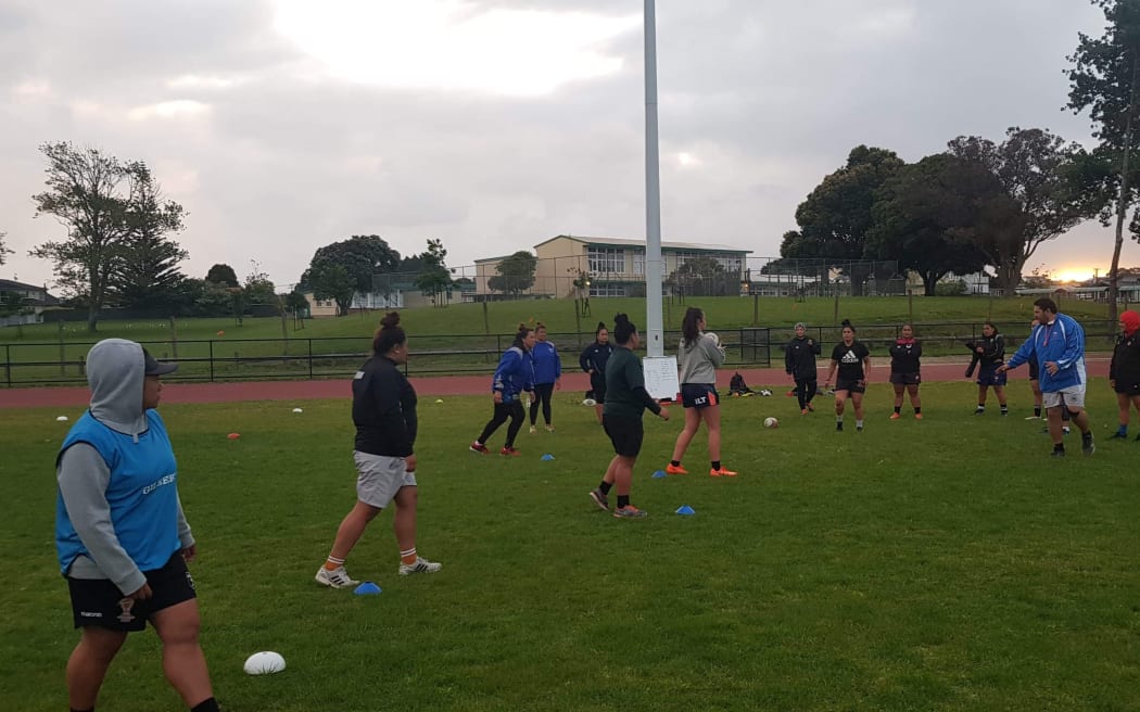 A photo of a traaining session for the Manusina - the Samoan Women's rugby team. There are about 12 players on the field being directed by a coach.