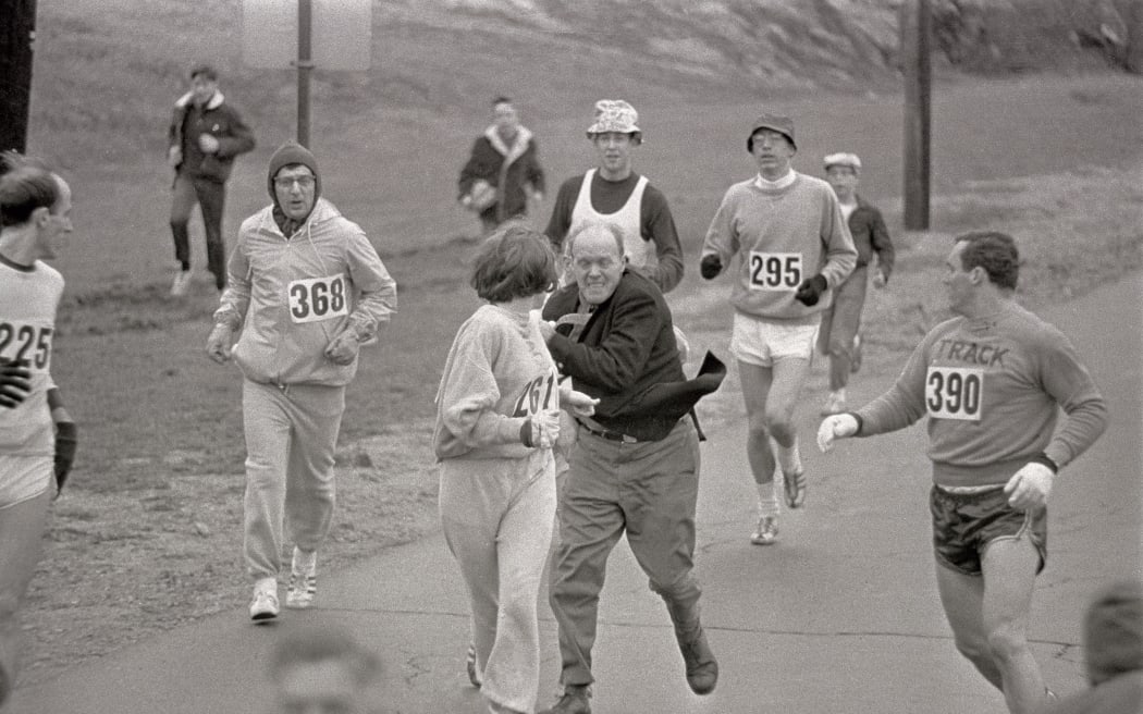 American marathon runner Katherine Switzer, who was the first woman to run the Boston Marathon as an officially registered competitor in 1967, and a trainer races after her to try and pull her off the track.