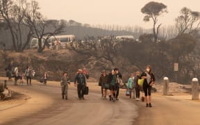 This handout photo taken on January 3, 2020 and released by the Royal Australian Navy shows people walking to a beach before being evacuated from Mallacoota, Victoria state to HMAS Choules, during bushfire relief efforts.