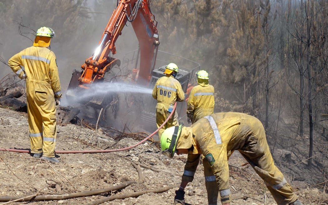 Men in hard hats and yellow jumpsuits with digger on firebreak alongside treesamonst