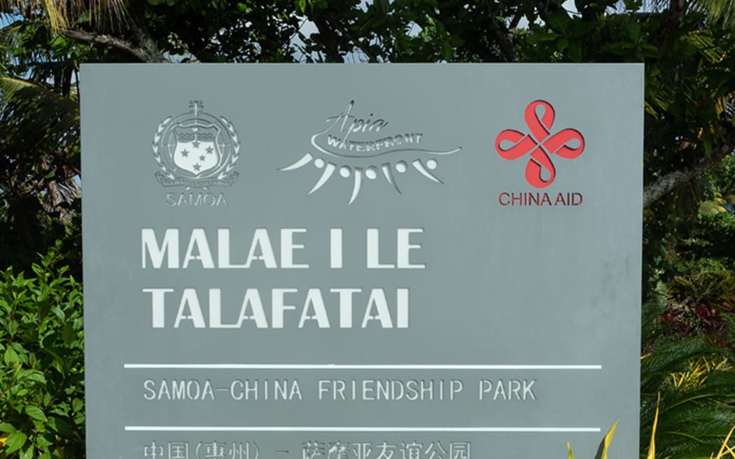A large grey welcome sign with white text, surrounded by gardens. It reads: 