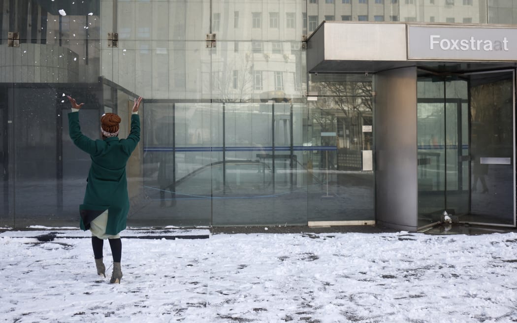 A woman throws snow in the air at a plaza in front of a Johannesburg office building, 10 July 2023.