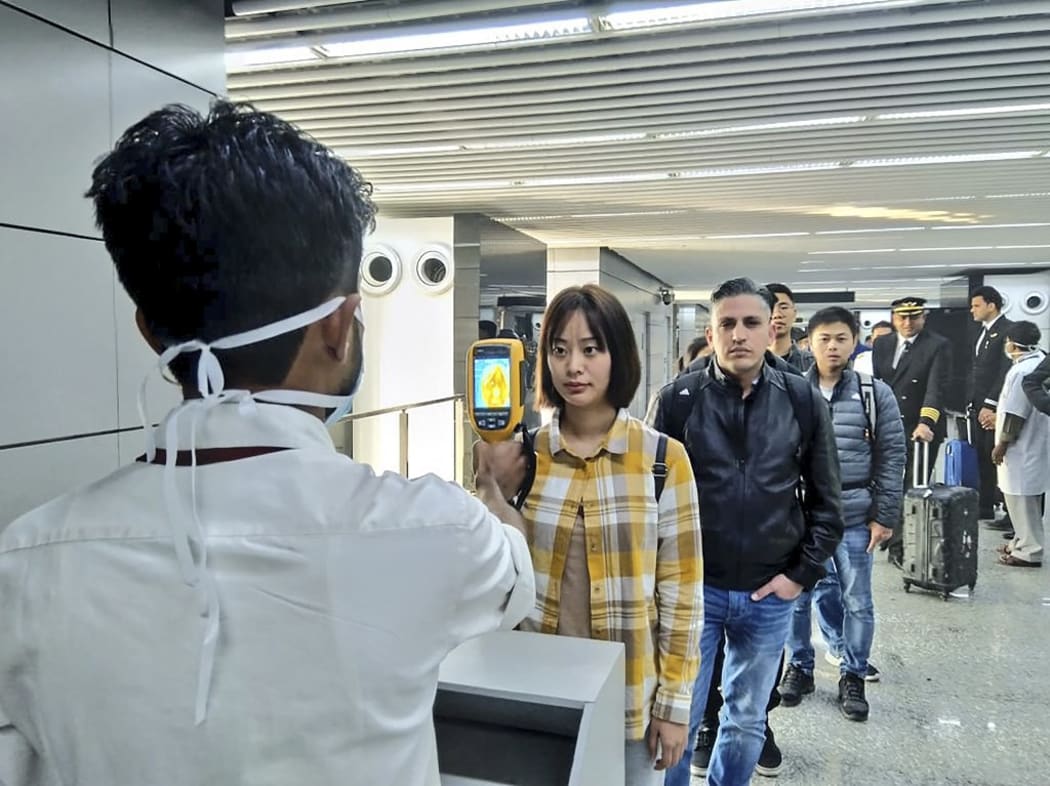 In this handout photograph taken and released by the Ministry of Civil Aviation (MoCA) on January 21, 2020, a man (L) uses a thermographic camera to screen the head of people at Netaji Subhash Chandra Bose International Airport in Kolkata.