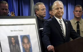 US Attorney Nick Hanna stands next to photos of Mark Steven Domingo during a news conference.