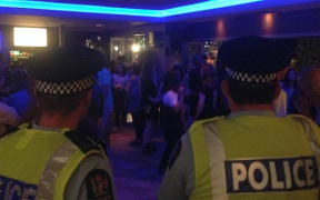 Two police officers in uniform look on as clients dance at night in bar
