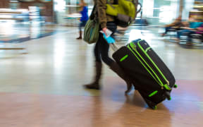 A woman with a backpack pulls a suitcase through an airport.