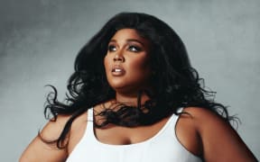 Image of Lizzo in a white vest top, hair blowing to the side, Bee Gees style.