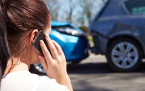 A woman makes a phone call, looking at a minor accident between two cars.
