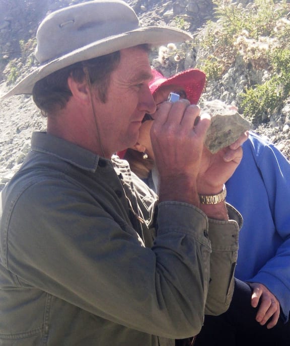 Trevor Worthy inspects a small animal bone embedded in a piece of rock.
