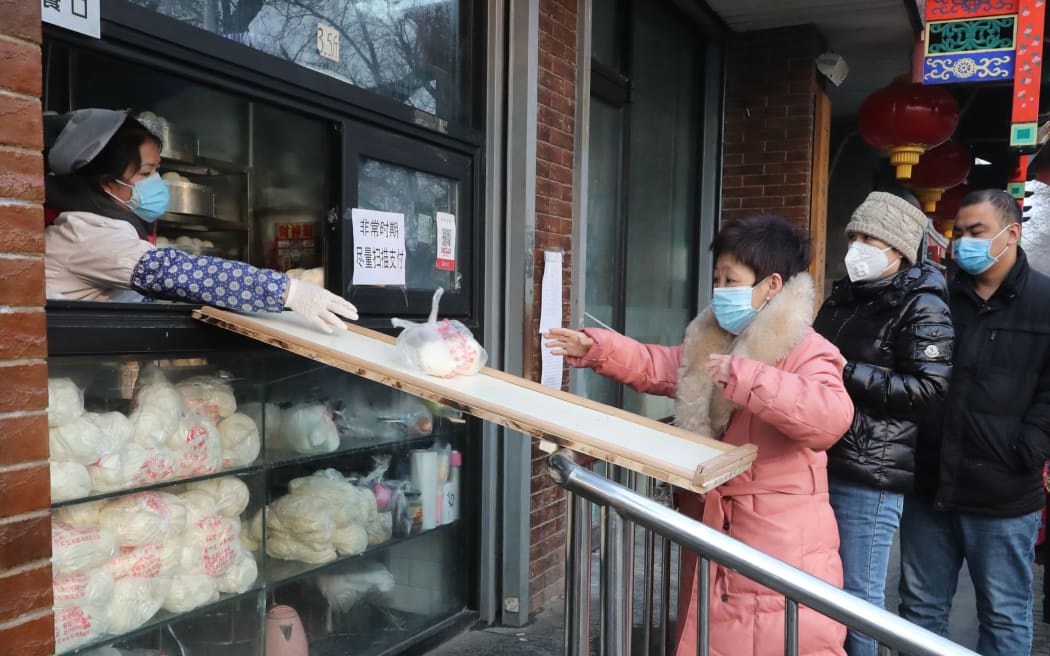 Shop staff uses a board to hand mantous, Chinese steamed bun, to customer in Beijing on February 11, 2020.