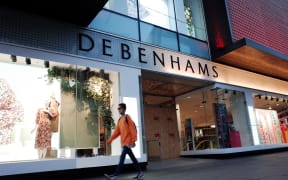 A woman walks past the boarded-up flagship branch of department store chain Debenhams on a near-deserted Oxford Street in London, England, April 2020.