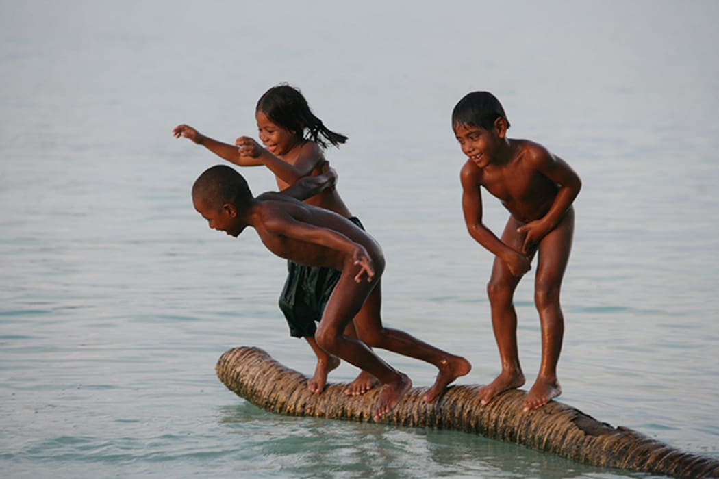 Children in Kiribati play on a partially submerged coconut trunk.