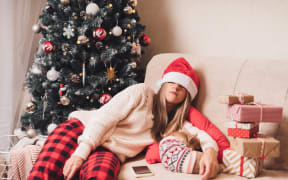Woman falling asleep and tired of gift wrapping with puppy dog on a couch in the living room with Christmas tree at home