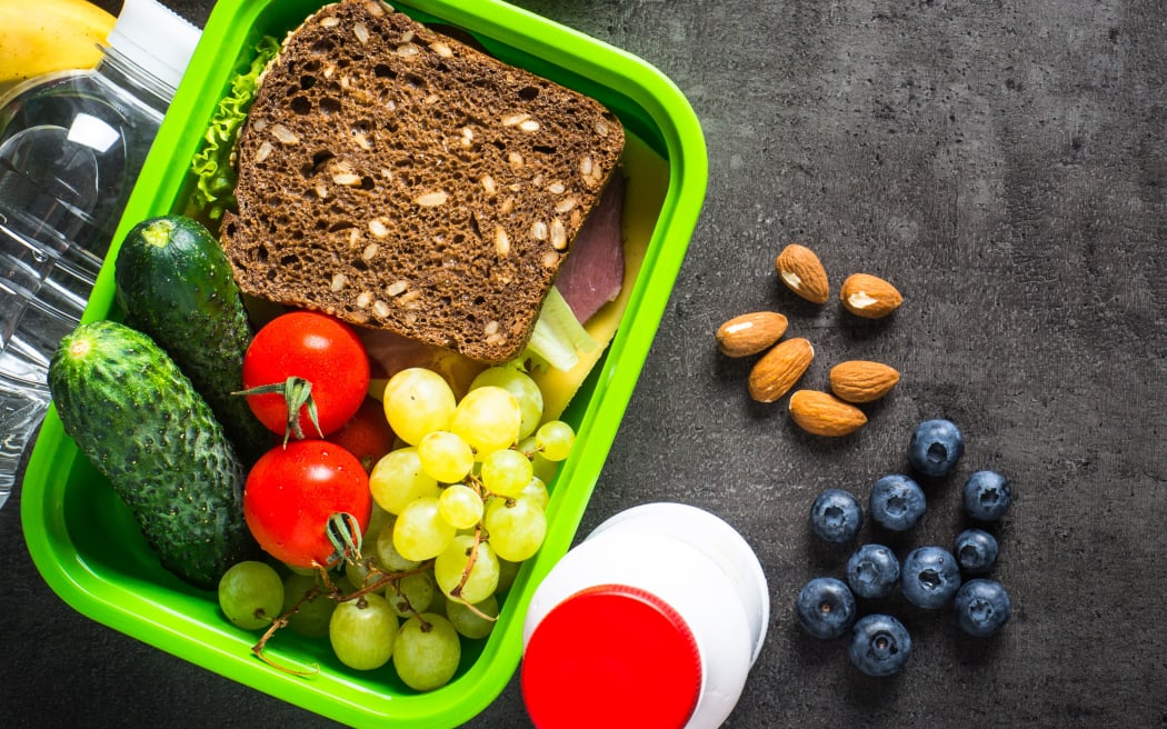 Lunch box with sandwich, fruit, vegetables, water.. Top view with copy space on black background.