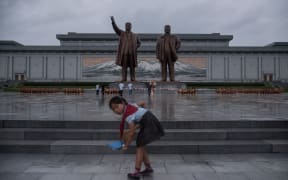A young girl cleans steps as people bow before the statues of late North Korean leaders Kim Il-Sung and Kim Jong-Il in Pyongyang.
