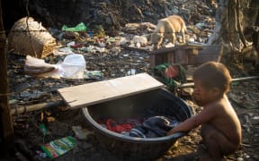 A child washes his face with laundry water among the trash and dogs in Tondo Landfill, Manila