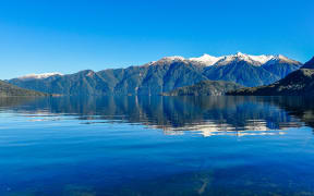 Reflection of snowy mountains in Lake Hauroko in the Southern Scenic Route, New Zealand
