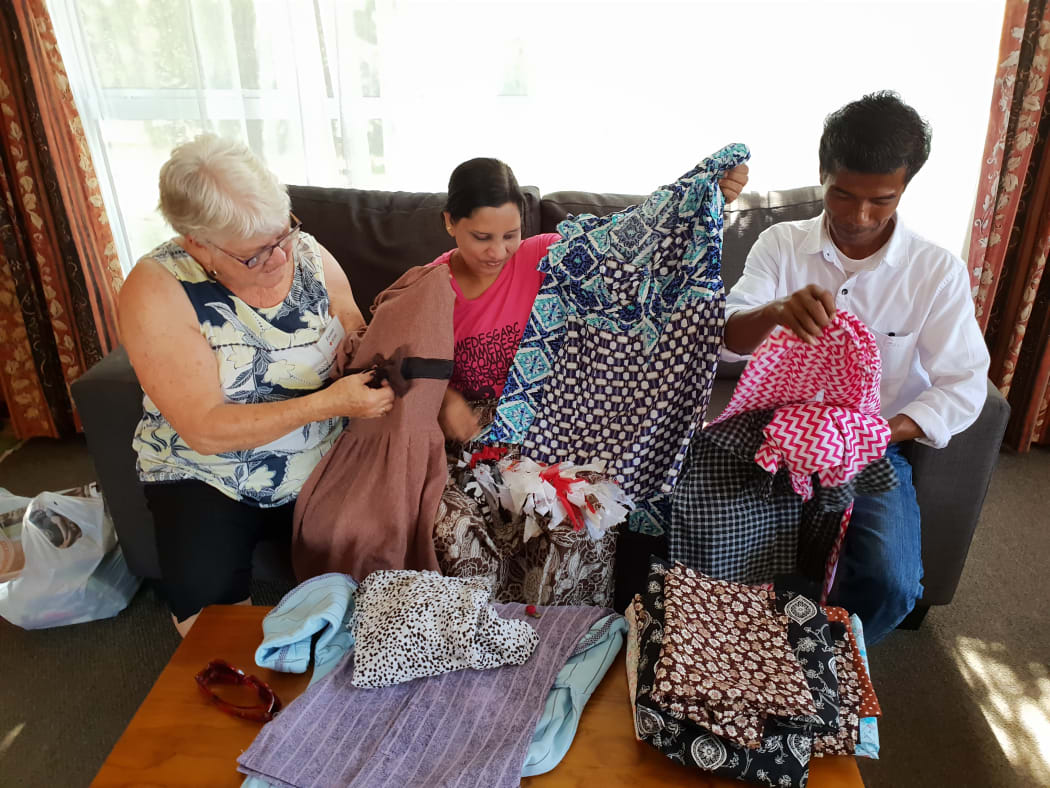 Shenenas Norbasha (centre) showing her creations she's made since receiving the sewing machine from the Red Cross. Pictured with her husband Mohammad (right) and the family's Red Cross volunteer, Esmee Rowden (left).