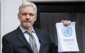 Wikileaks founder Julian Assange speaks from the balcony of the Ecuadorian embassy, holding up the UN Panel's decision.