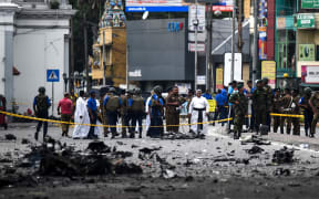 Sri Lankan security personnel inspect the debris of a car after it explodes when police tried to defuse a bomb near St. Anthony's Shrine as priests look on in Colombo on April 22, 2019, a day after the series of bomb blasts targeting churches and luxury hotels in Sri Lanka.
