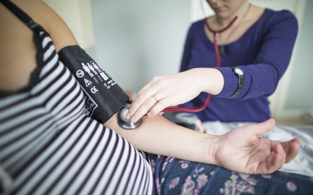 Stock image. Midwife examining pregnant woman at home.