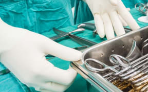 A surgeon in scrubs and white gloves with a tray of instruments.