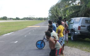 Children watch as a small plane comes in to land at Funafuti airport in Tuvalu.