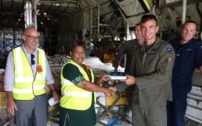 Flight Lieutenant Kendall Dooley, the captain of the Royal New Zealand Air Force hands over the textbooks to Merewalesi Vueti, the Director of Library Services in Fiji’s Ministry of Education, as New Zealand High Commissioner to Fiji Mark Ramsden (left) looks on.