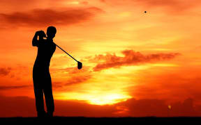 13224828 - male golfer hit golf ball toward the hole at sunset silhouetted