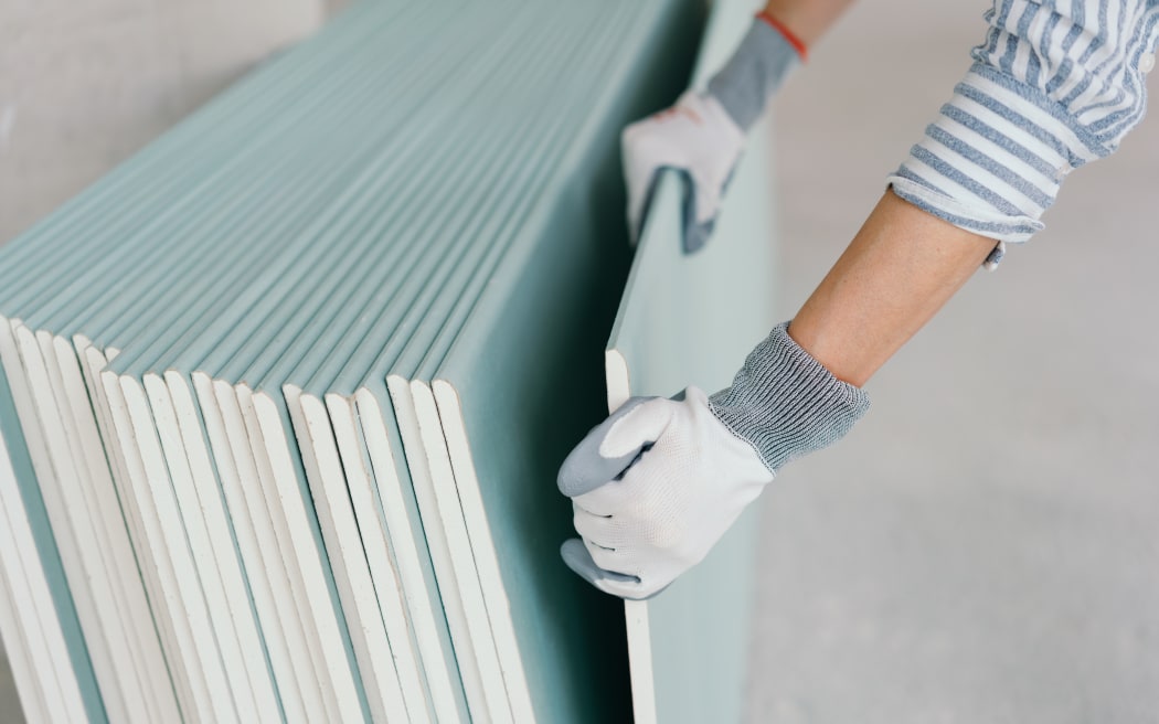 Person wearing protective gloves grabbing a sheet of chip board for use in interior building construction in a close up on the hands